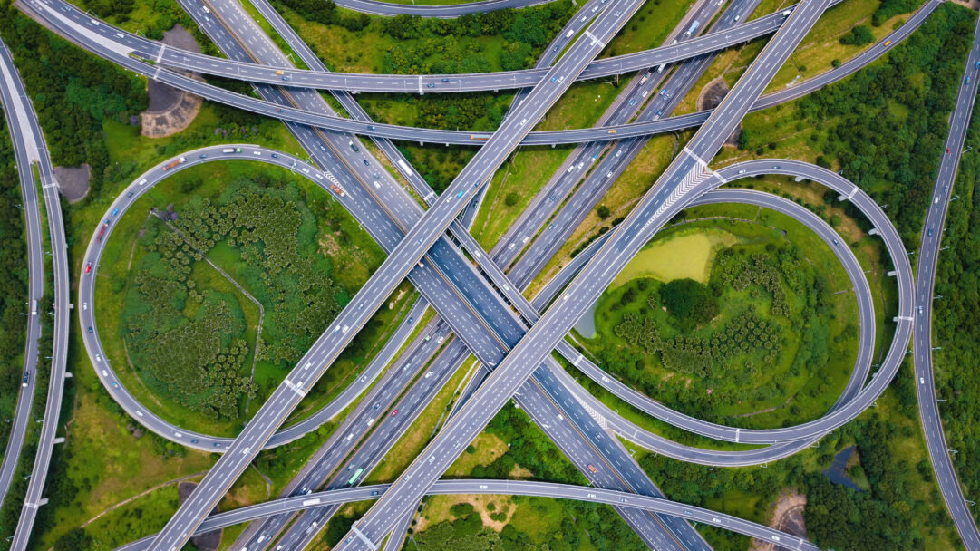 An intricate 4K wallpaper showcasing an aerial view of a sprawling highway interchange in Taipei, Taiwan, where numerous elevated roads weave across a vibrant green landscape. Vehicles move steadily along the complex network of grey asphalt, creating a dynamic visual interplay with the surrounding lush natural environment.