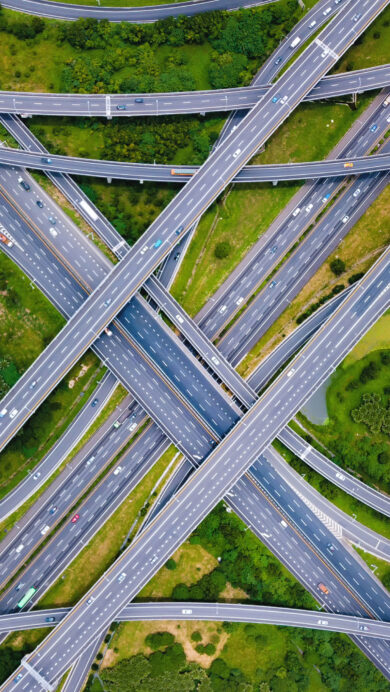 An intricate 4K wallpaper showcasing an aerial view of a sprawling highway interchange in Taipei, Taiwan, where numerous elevated roads weave across a vibrant green landscape. Vehicles move steadily along the complex network of grey asphalt, creating a dynamic visual interplay with the surrounding lush natural environment.