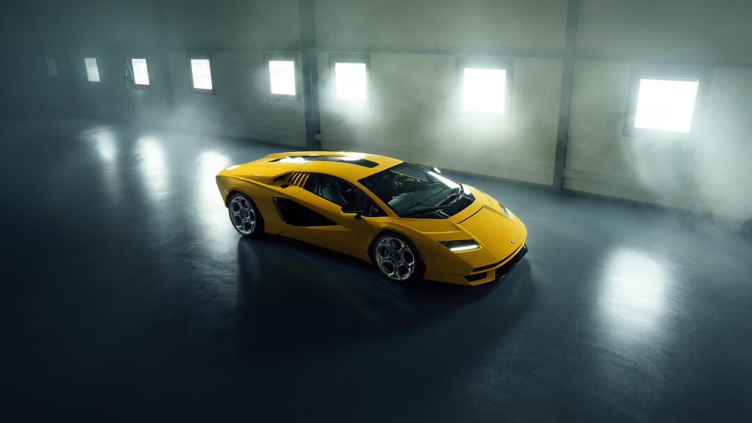 A dramatic 4K wallpaper of a vibrant yellow Lamborghini Countach parked centrally in a vast, dimly lit garage. The vibrant yellow car is dramatically lit, casting reflections on the dark floor, as soft, ethereal haze filters brilliant light from high windows, creating a mysterious and powerful atmosphere.