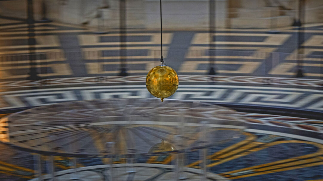A mesmerizing 4K wallpaper of the Golden Foucault Pendulum suspended within the grand interior of the Panthéon in Paris, France. Its polished golden sphere shines brightly, reflecting the intricate geometric patterns of the Panthéon's floor and evoking a sense of scientific wonder and perpetual motion.