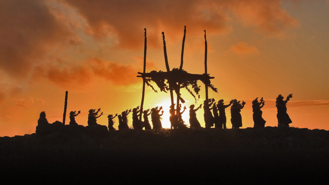 A spiritual 4K wallpaper captures silhouetted Hawaiian dancers performing at a Lele Altar on Mount Maunaloa, Molokai, against a vivid sunset. The intense orange and gold sky dramatically backlights the figures and the altar, creating a serene and powerful cultural atmosphere.