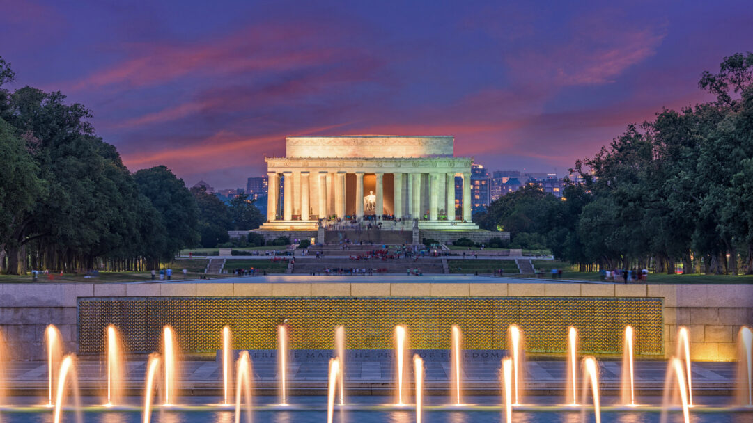 A breathtaking 4K wallpaper presents the iconic Lincoln Memorial and World War II Memorial in Washington D.C., viewed at sunset with the vibrant Rainbow Pool fountains in the foreground. The warm golden glow of the fountains contrasts beautifully with the deep purples and oranges of the twilight sky, highlighting the solemn beauty of these historic landmarks.
