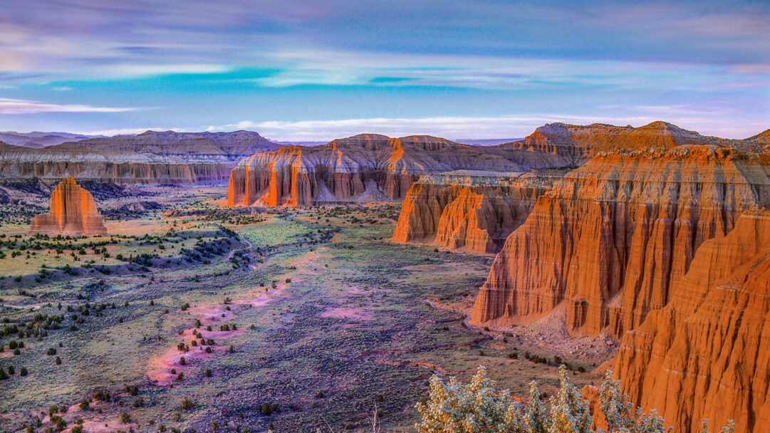 A breathtaking 4K wallpaper captures Mesas in Upper Cathedral Valley of Capitol Reef National Park, Utah, extending across a vast, rugged desert landscape. Golden light intensely illuminates the towering red rock formations, contrasting sharply with the cooler, shadowed valley floor and the dramatic, multi-hued sky above.