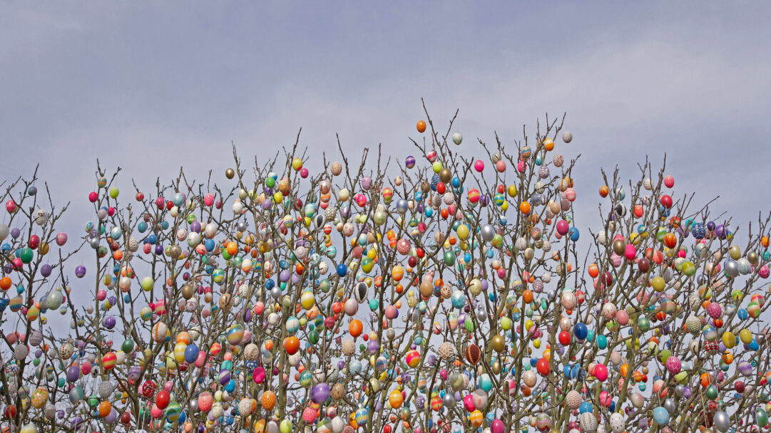 A vibrant 4K wallpaper showcasing the famous Ostereierbaum (Easter Egg Tree) in Saalfeld, Germany, where bare tree branches are densely covered with an abundance of Easter eggs. Hundreds of meticulously decorated eggs in diverse colors and patterns create a dazzling, joyful spectacle against a light, overcast sky.