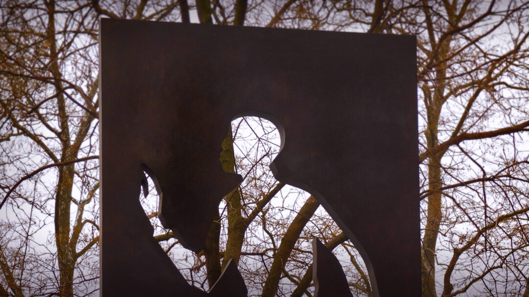 A poignant 4K wallpaper features the Ralph Ellison Memorial Sculpture situated in New York City's Riverside Park. The monumental dark metal form, with its distinctive human profile cut-outs, starkly frames the delicate network of bare winter tree branches against a bright, muted sky, evoking a sense of profound remembrance.