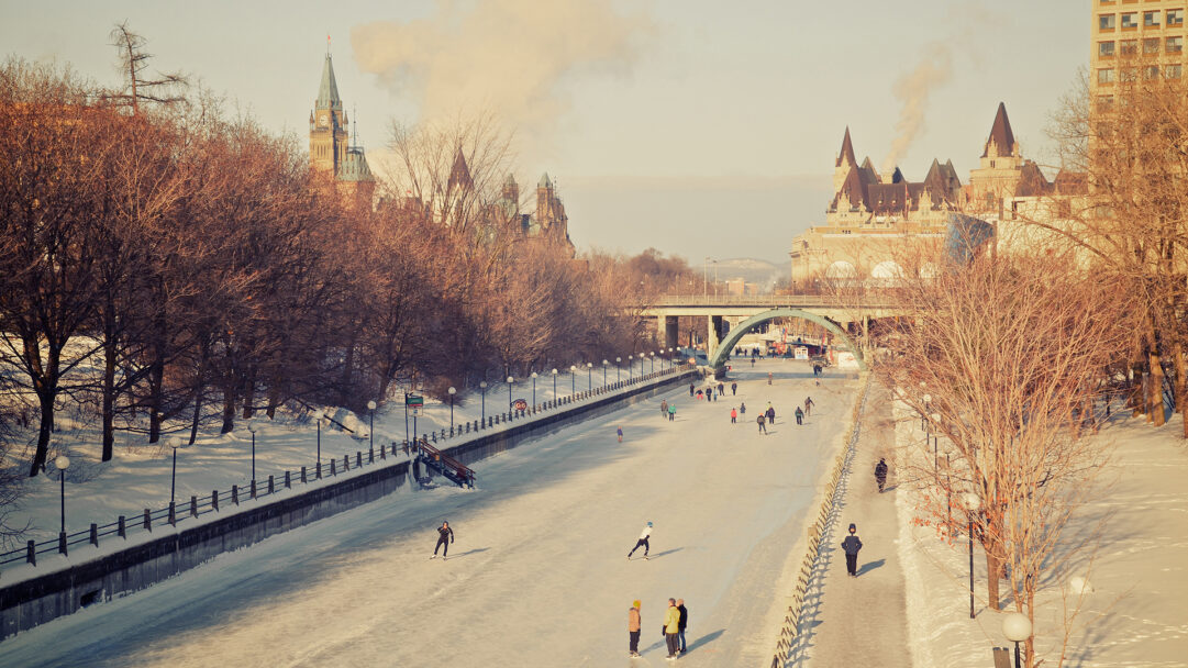 A charming 4K wallpaper of the Rideau Canal Skateway during Winterlude in Ottawa, Canada, showing numerous people enjoying winter skating. Golden sunlight bathes the frozen canal and surrounding historic architecture, creating a nostalgic mood as skaters glide along the popular urban ice route.