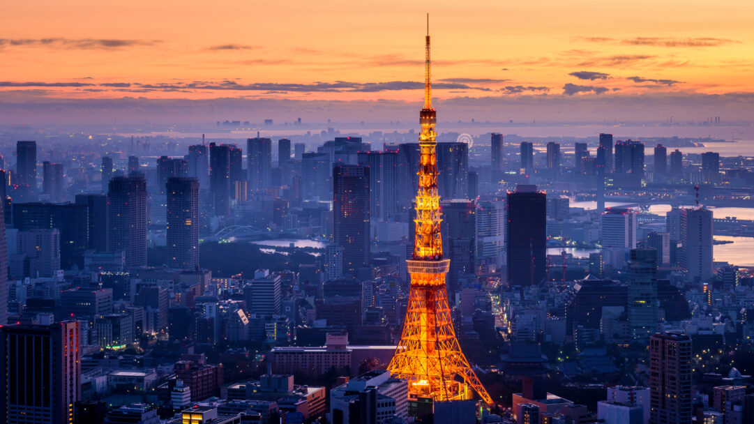 A captivating 4K wallpaper showcases the iconic Tokyo Tower, brilliantly lit, against the sprawling Minato City skyline of Japan at sunset. Its radiant orange glow dramatically contrasts with the twilight sky's soft orange and purple palette, as the city's myriad lights begin to twinkle in the cool blue dusk.