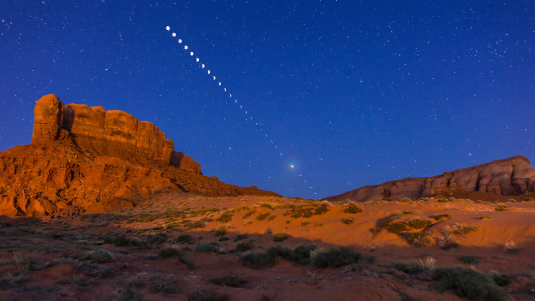 A celestial 4K wallpaper showcasing a Total Lunar Eclipse unfolding as a time-lapse across a vast desert night sky. The moon’s progression from crescent to a dramatic red ‘blood moon’ forms a captivating arc above the rugged, warmly illuminated desert formations, bathed in the starry blue expanse of the night.