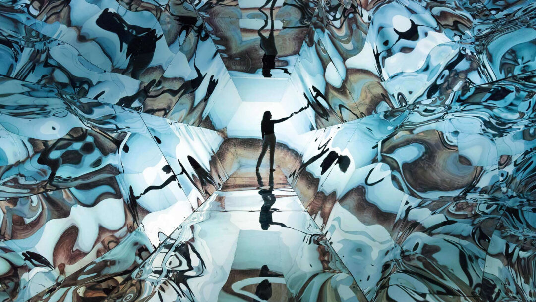 A captivating 4K wallpaper showcasing Artist Laura Buckley's mixed media sculpture, an abstract reflections installation forming an immersive, kaleidoscopic tunnel where a silhouetted figure stands reaching out. The interplay of light on the undulating, mirrored surfaces generates mesmerizing blue and brown abstract patterns, creating an otherworldly and exploratory mood.