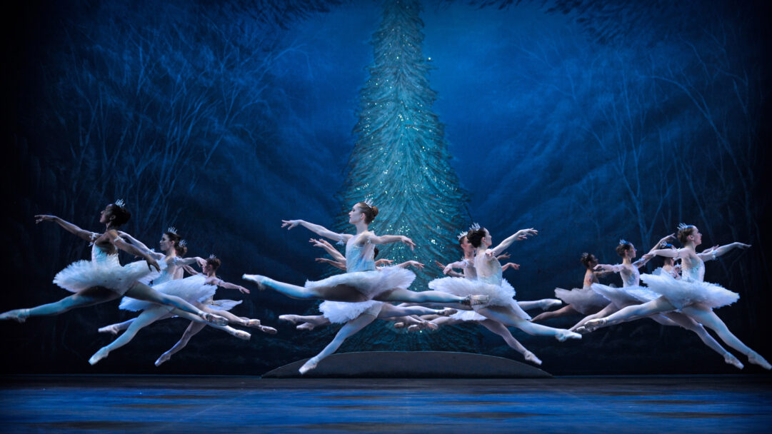 A magical 4K wallpaper of the English National Ballet's 2016 Nutcracker production shows several ballerinas in white tutus performing a synchronized leap on a dark stage. The deep blue lighting illuminates a twinkling, stylized Christmas tree and frost-laden forest backdrop, creating an ethereal winter wonderland mood.