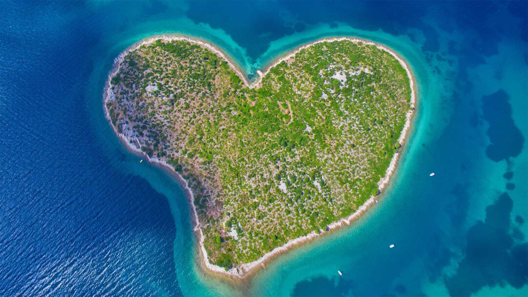 A captivating 4K wallpaper showcases Galešnjak Island, an iconic heart-shaped landmass, floating majestically in the clear azure waters of the Adriatic Coast. The island's verdant, scrub-covered terrain is sharply outlined by bright turquoise shallows that gradually deepen into the breathtaking sapphire blue of the surrounding sea, emphasizing its unique and romantic form.