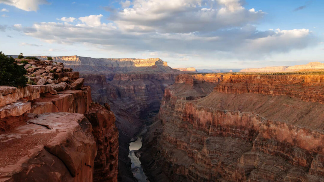 A majestic 4K wallpaper reveals the Grand Canyon's vast expanse from the Toroweap Overlook, with the Colorado River winding through its depths. Golden sunset light illuminates the upper rim and distant mesas, creating a vibrant contrast against the deep shadowed layers of the canyon below.