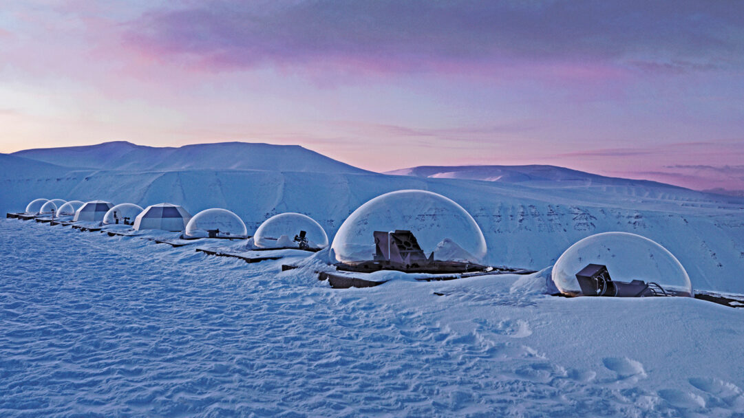 A breathtaking 4K wallpaper showcases the Kjell Henriksen Observatory's scientific domes lining a pristine, snow-laden winter landscape in Svalbard, Norway. The dramatic contrast between the frigid, expansive snow and the sky's vibrant purples and pinks evokes a sense of serene isolation.
