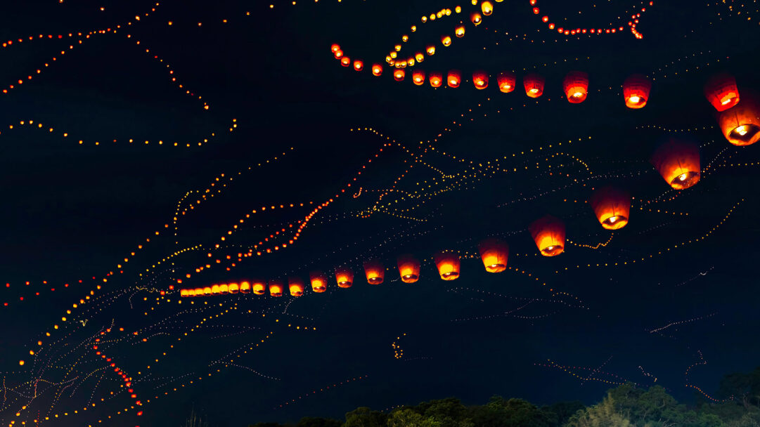 A magical 4K wallpaper of the Pingxi Taiwan Lantern Festival night sky, where numerous glowing sky lanterns ascend into the darkness. The bright orange and yellow lanterns, some leaving streaking trails of light, create a breathtaking, hopeful spectacle against the deep blue-black heavens.