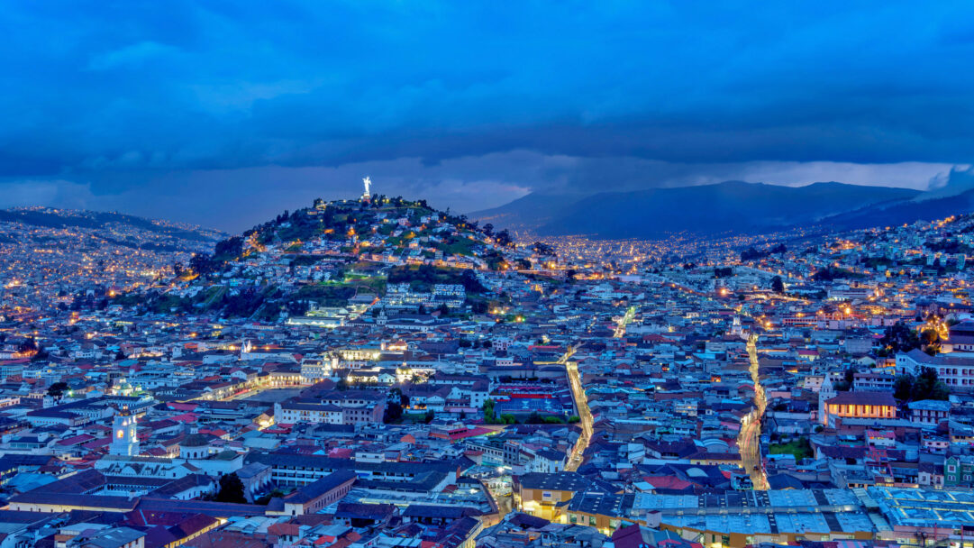 A breathtaking 4K wallpaper showcasing the sprawling Old Town cityscape of Quito, Ecuador, at night, with El Panecillo Hill centrally dominating the view. Thousands of warm city lights illuminate the historic district and cascade up the surrounding hills, with the iconic illuminated statue atop El Panecillo glowing majestically against the deep twilight sky.
