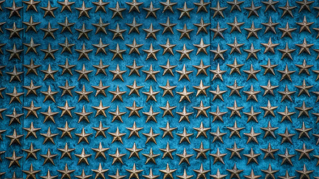 A poignant 4K wallpaper displaying the World War II Memorial Freedom Wall, covered in countless bronze stars arranged in neat rows. The weathered texture of the golden-bronze stars creates a striking contrast with the deeply textured, somber blue background, evoking a profound mood of solemn remembrance.